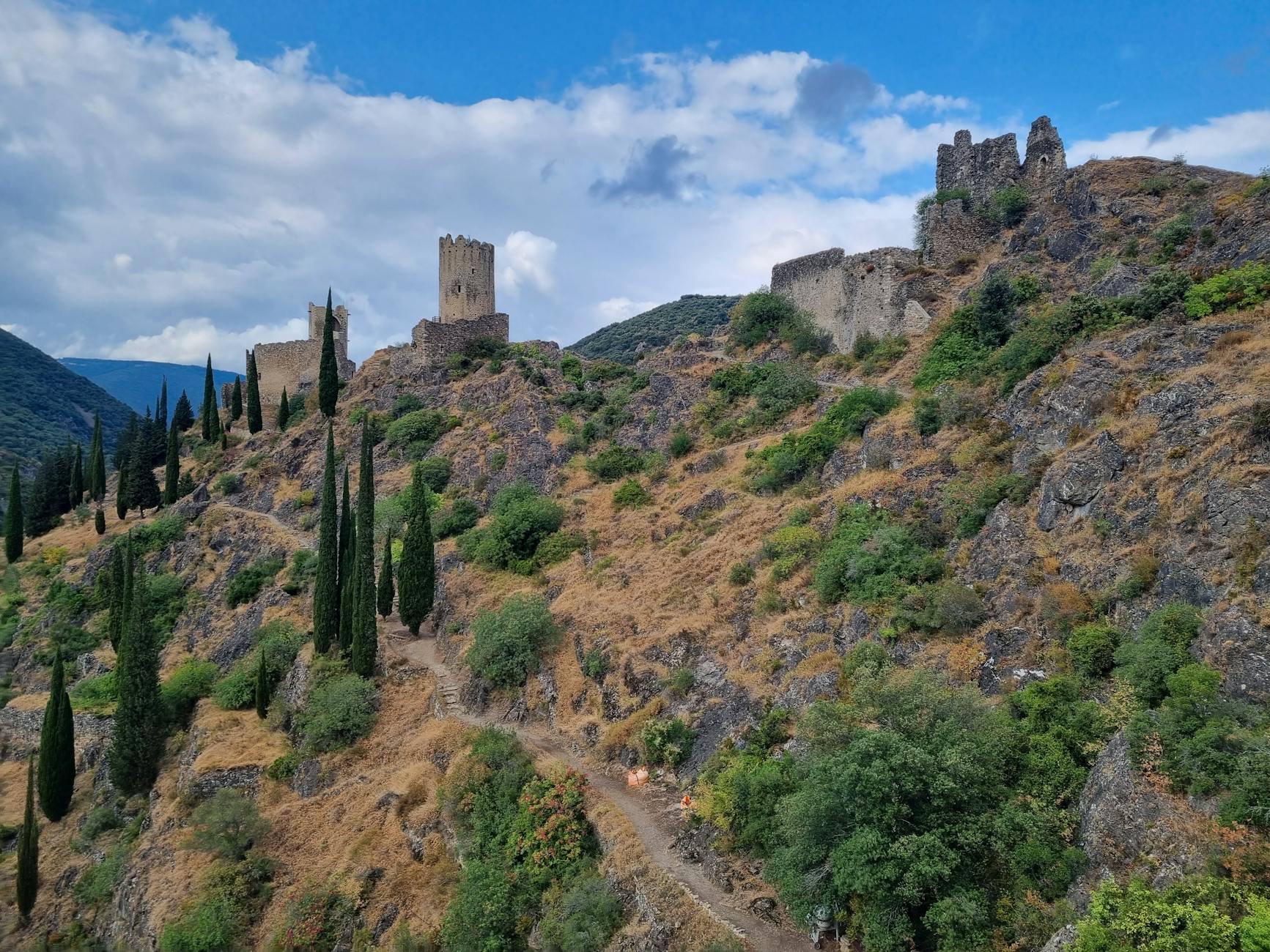 Ruiny starego zamku na skalistym wzgórzu wśród cyprysów i zieleni