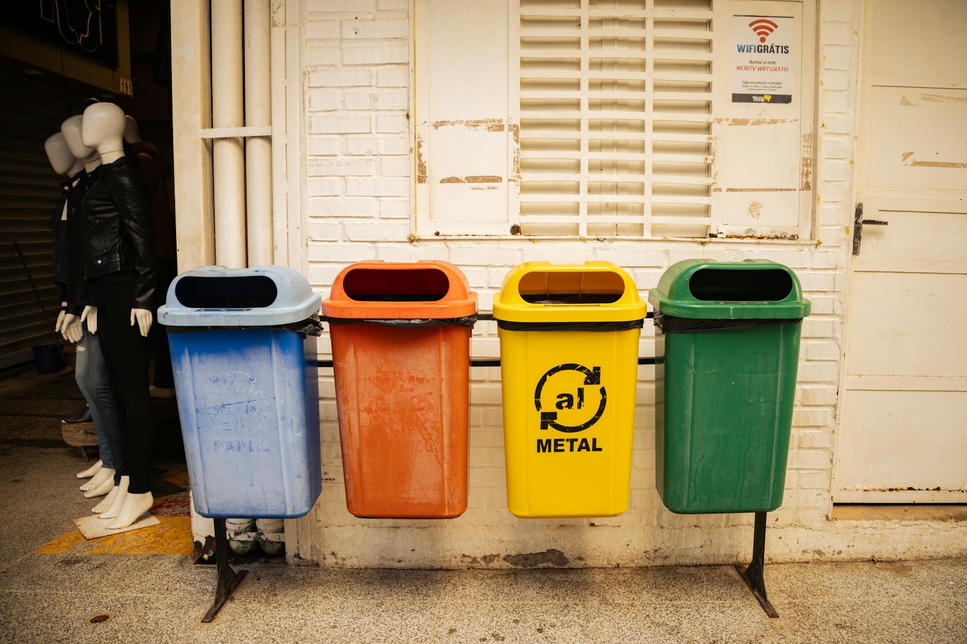 Cztery kolorowe pojemniki do segregacji odpadów na tle ceglanej ściany