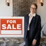 Agent nieruchomości w garniturze trzyma pustą tablicę na sprzedaż w mieszkaniu