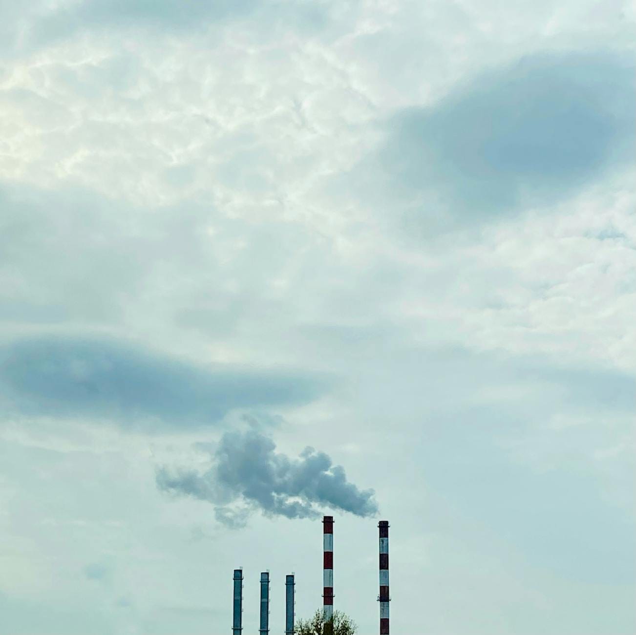 Kominy przemysłowe emitujące dym pod pochmurnym niebem