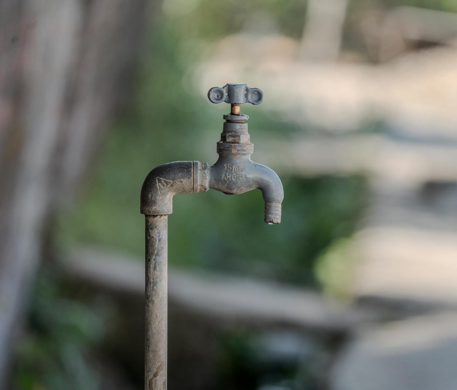 Zardzewiały zewnętrzny kran na tle zieleni, symbol oszczędzania wody