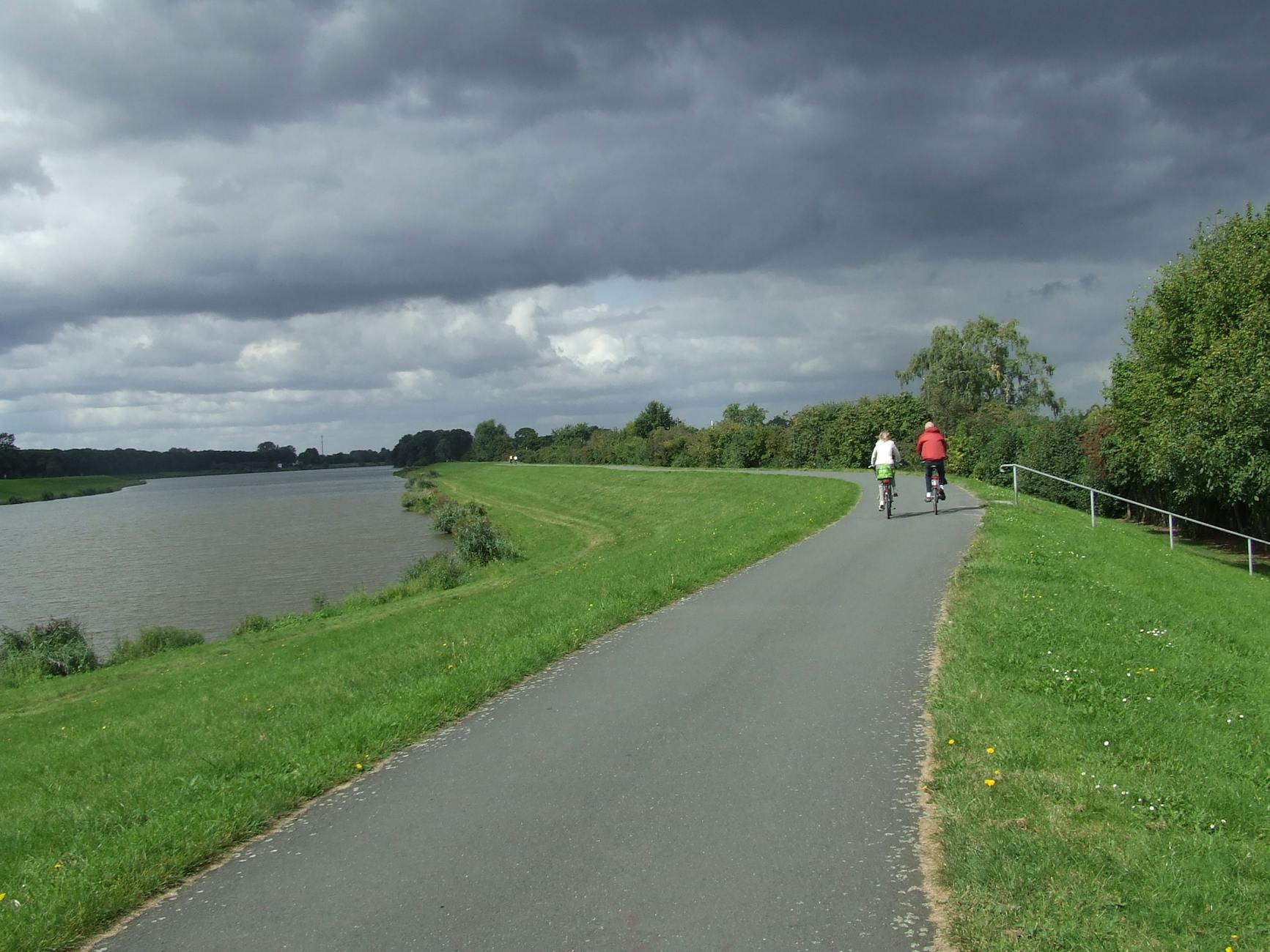 Dwóch rowerzystów na ścieżce nadwiślańskiej pod burzowymi chmurami